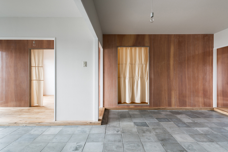 ハイツYの修理 既存の間取りをそのままに、居室を横断するように挿入した木質素材の壁のみで各室の関係性を変化させ、様々な居住形態に対応するものへと更新。挿入した壁の素材であるラワン合板表面に貼られた「IROMIZU」。合板という素材の特性である経年変化を透過しつつ、経過してゆく時間を可視化する。また、貼られたIROMIZUは室内外の風景の映り込みや光の反射を表面上で現象させる